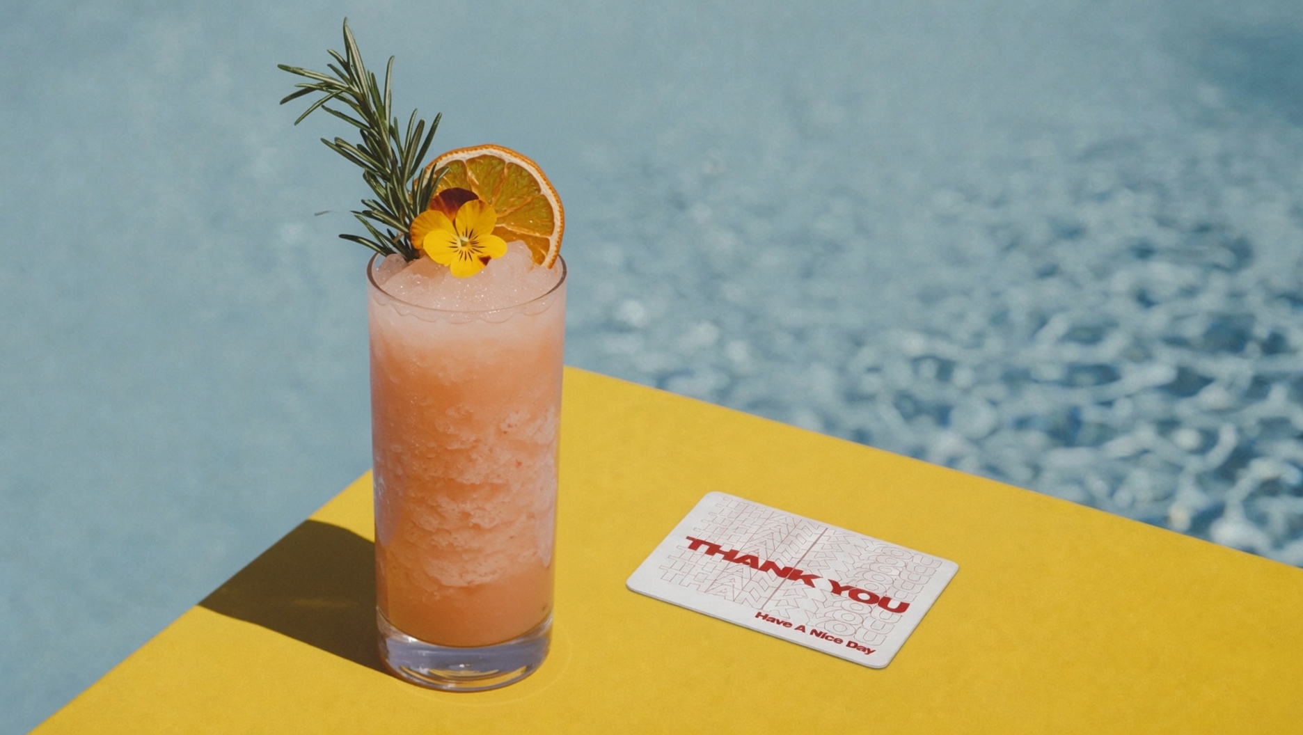 A white Thank You card with red outline type on a red poolside table beside a cocktail